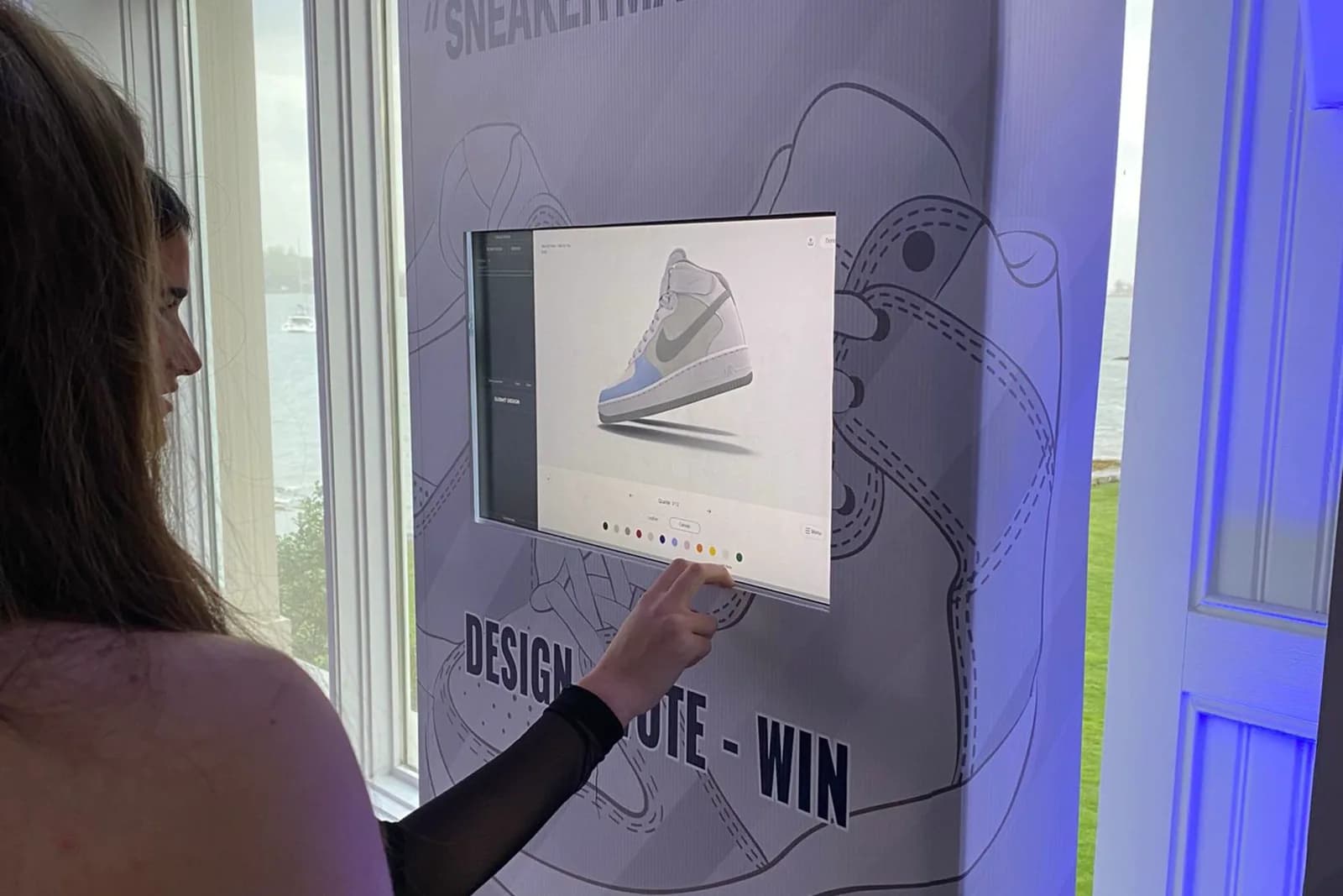 Guest selecting a color option on a sneaker design kiosk screen at an event overlooking the water