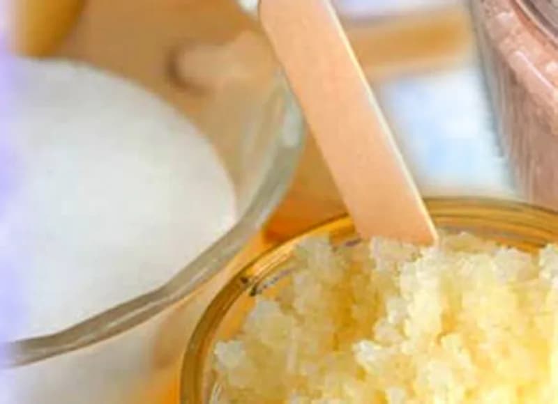 Jar of sugar scrub with a wooden mixing stick beside a bowl of granulated sugar, ingredients used at the sugar and salt scrub station