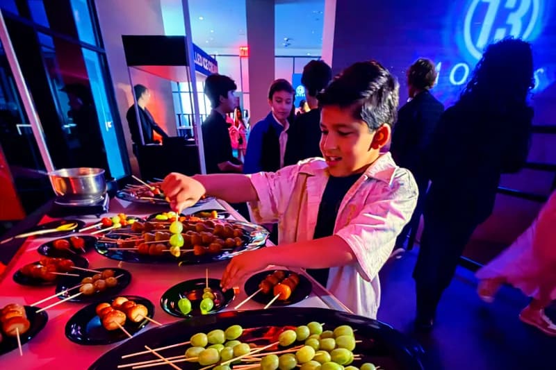 Guest at a bar mitzvah picking candied tanghulu grape and fruit skewers from a plated event station