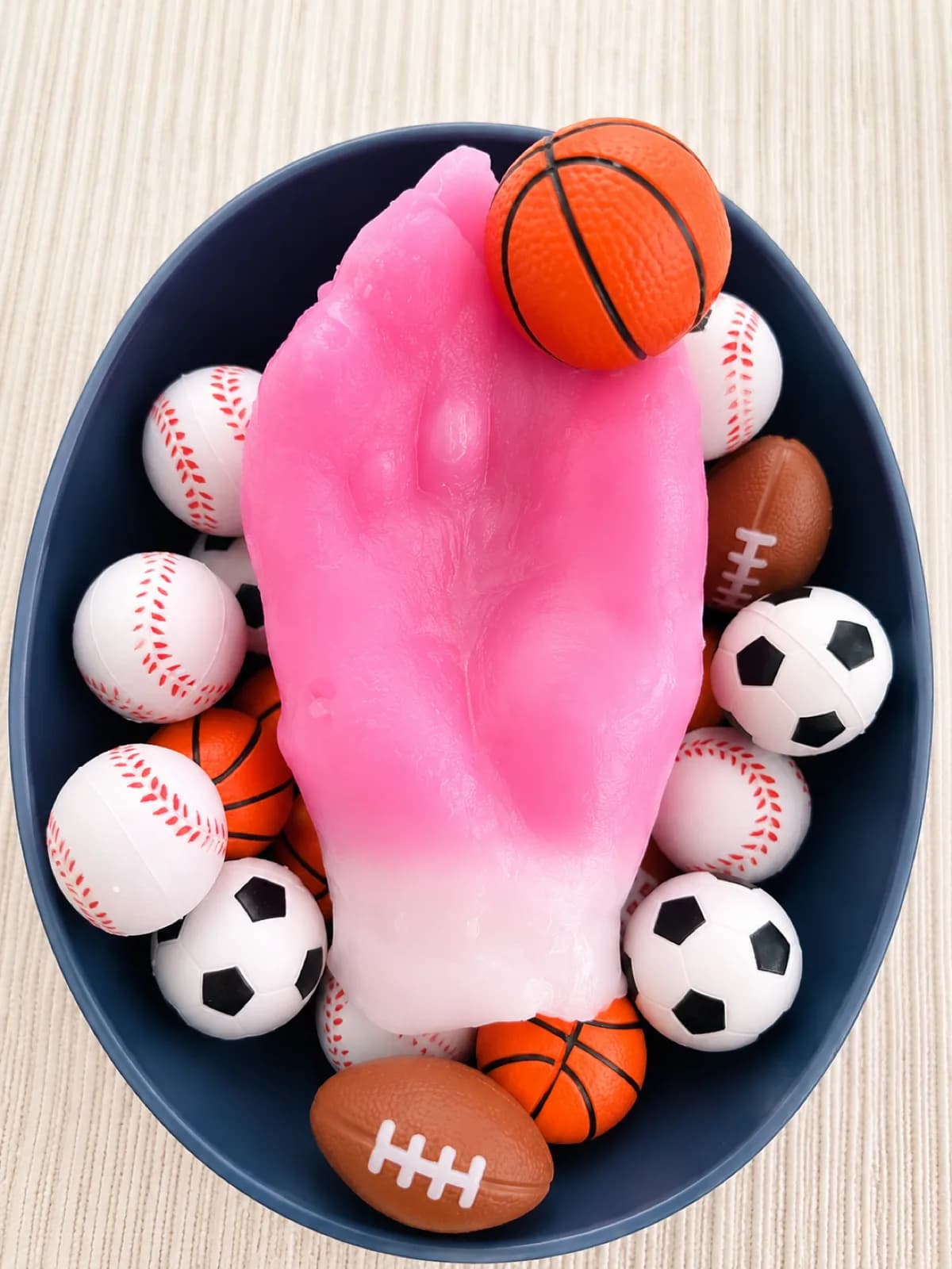 Pink wax hand cast nestled in a bowl of mini basketballs, baseballs, soccer balls, and footballs at a wax hands station