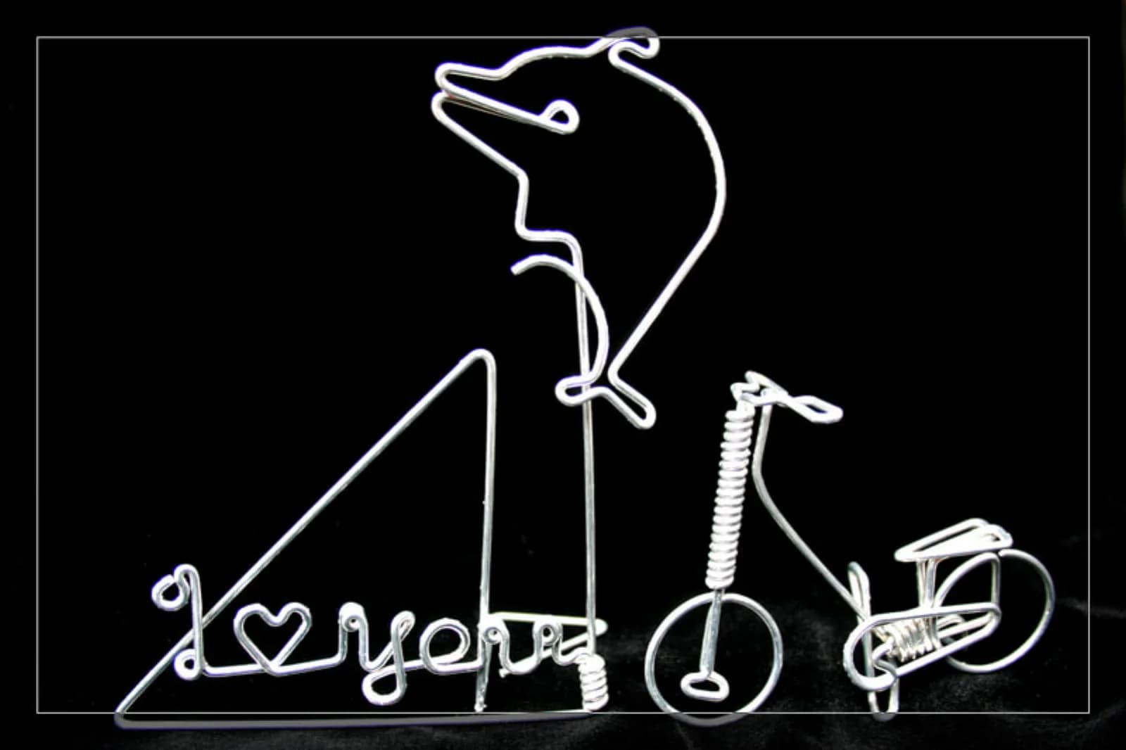 Wire art piece shaped like a leaping dolphin and a bicycle paired with a guest name, a keepsake from the wire art station