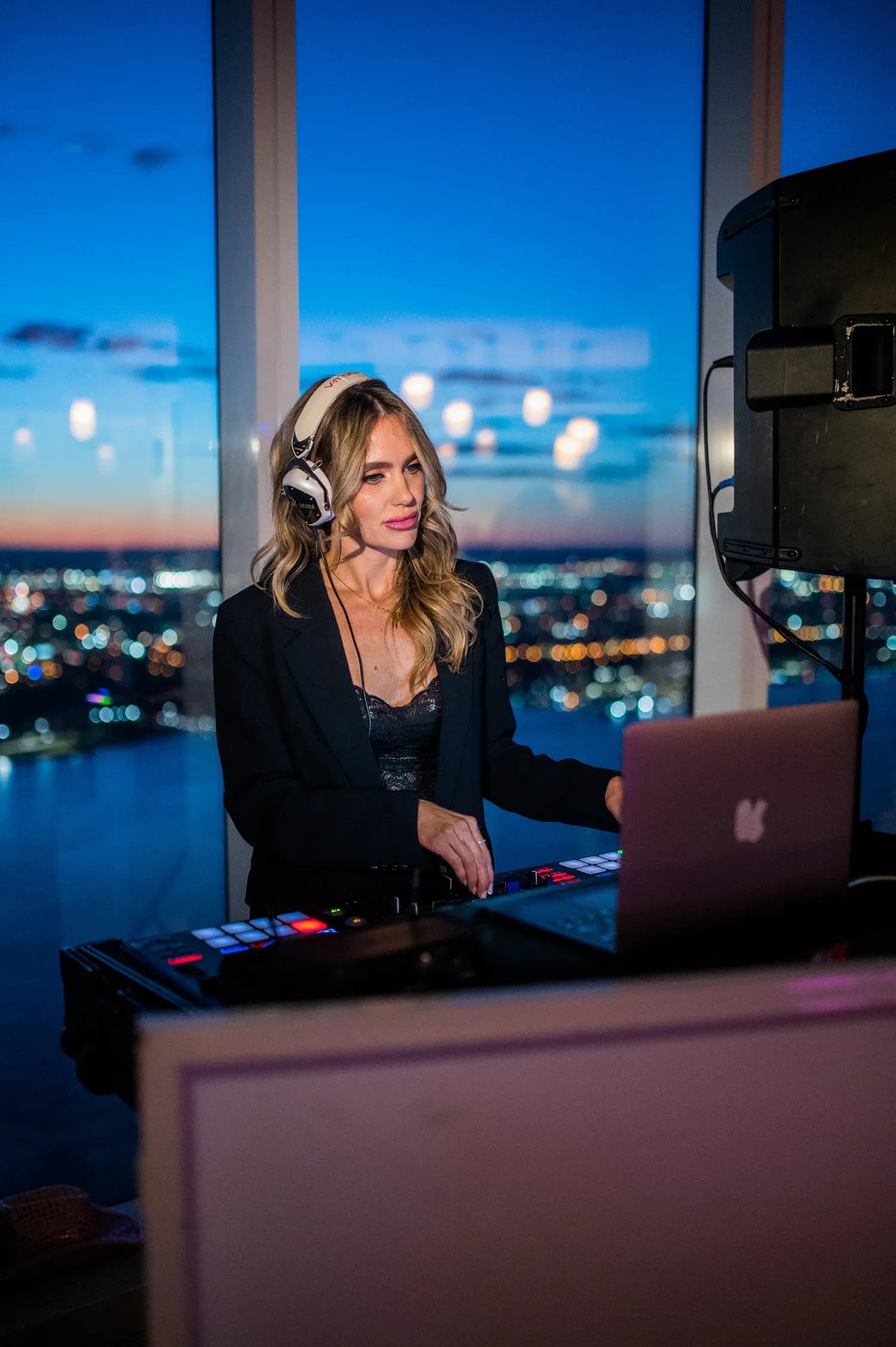DJ Dani at the decks with the NYC skyline lit up at night behind her