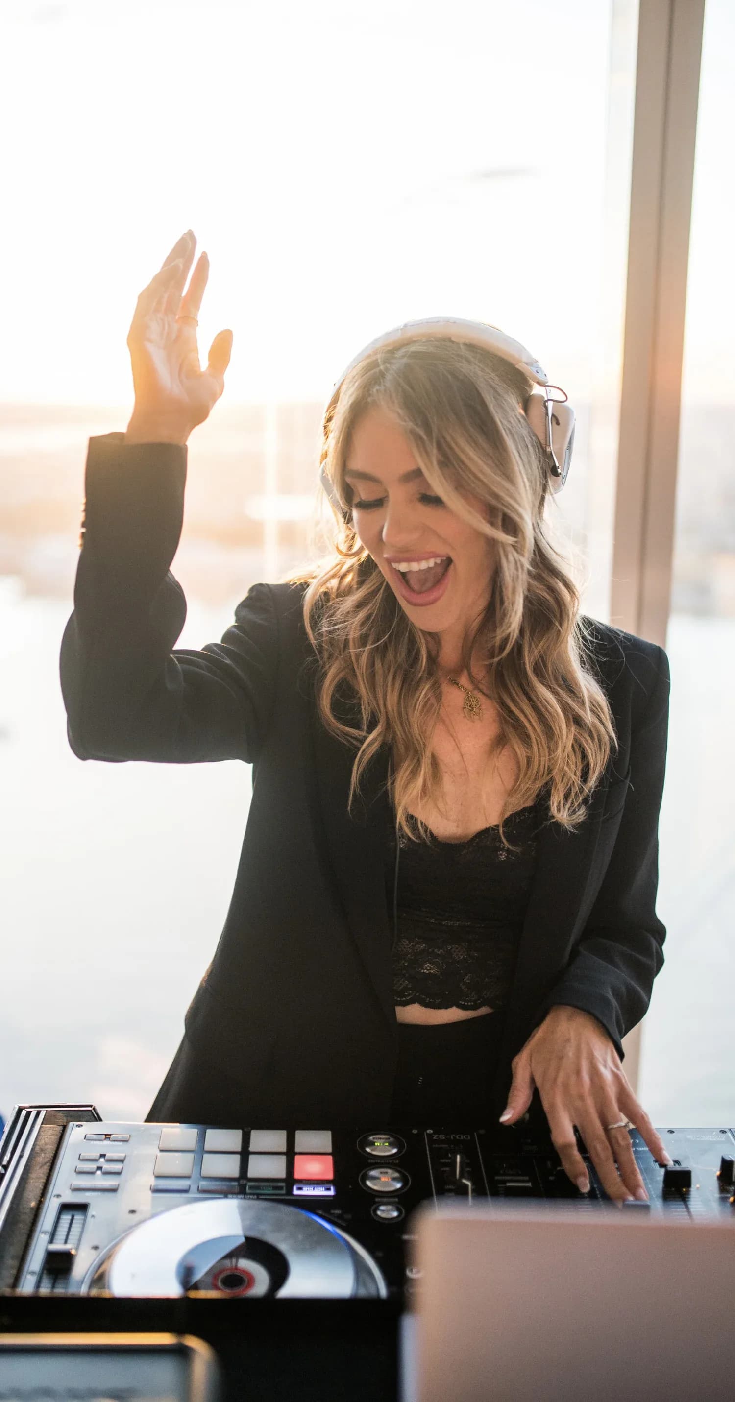DJ Dani laughing and performing energetically at the decks during a golden-hour high-rise event