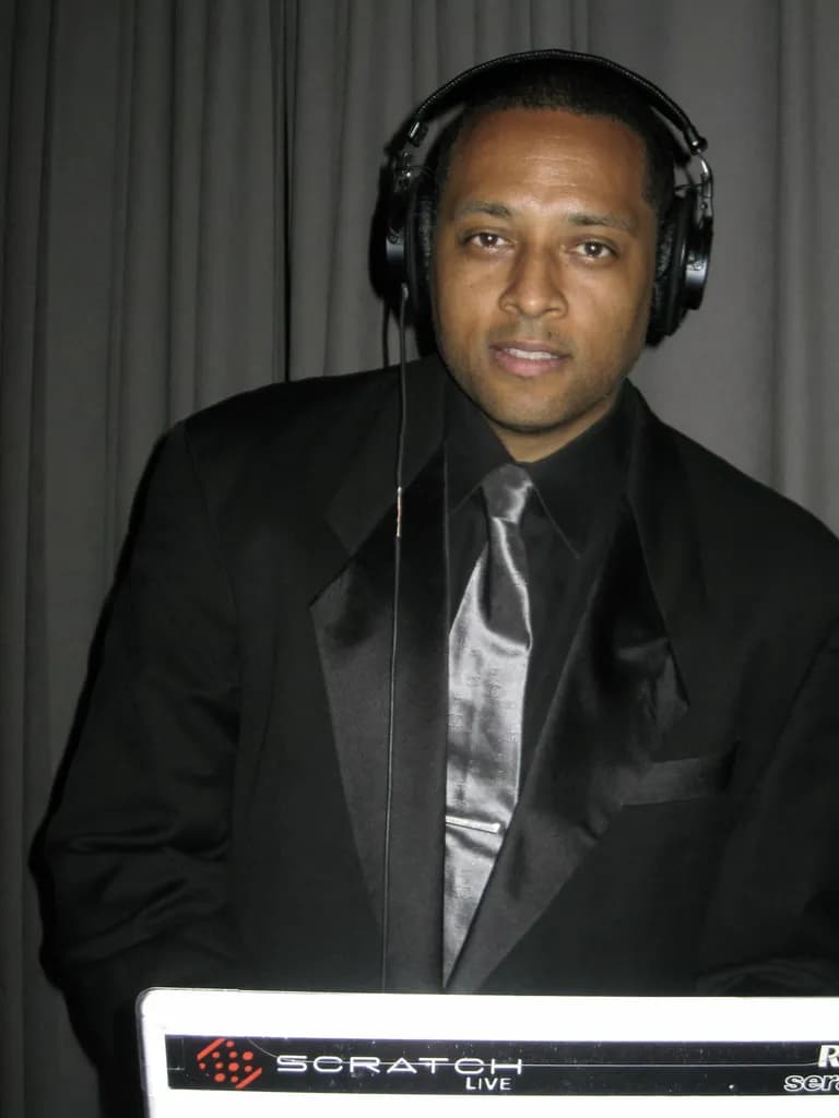 DJ David Raimer in a black tuxedo and silver tie at the booth, a polished formal portrait