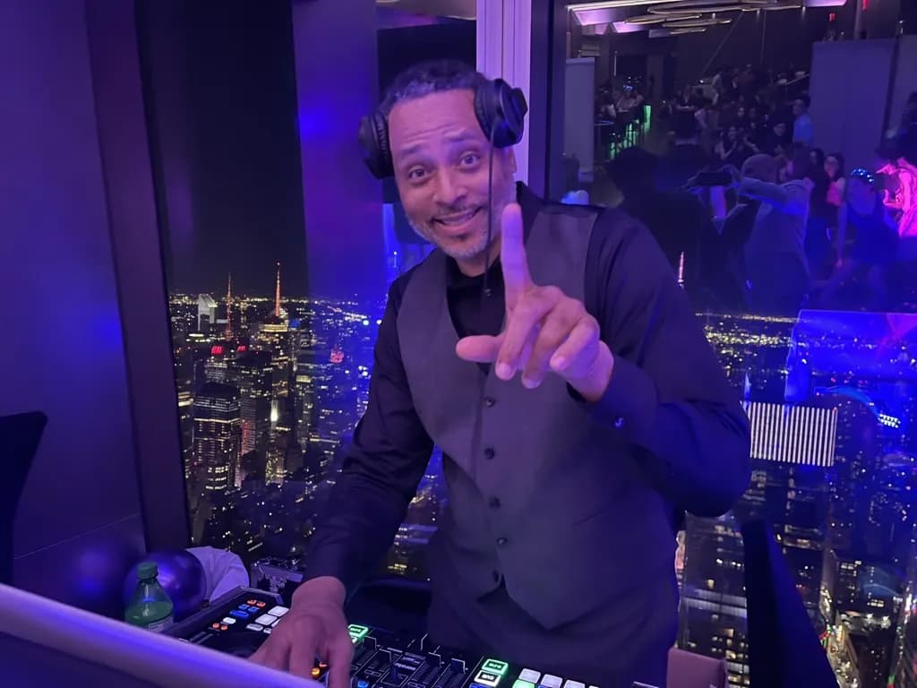 DJ David Raimer at the decks at a rooftop venue high above the Manhattan skyline at night