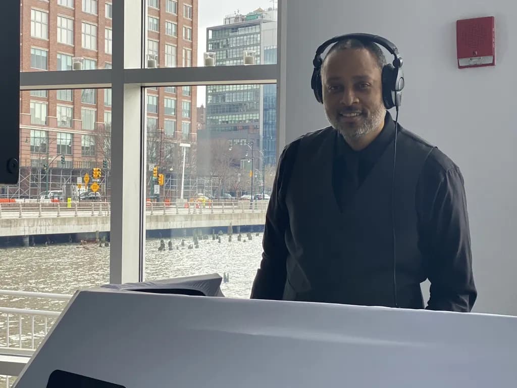 DJ David Raimer in a black vest and headphones at a waterfront loft venue overlooking the Hudson River in daylight
