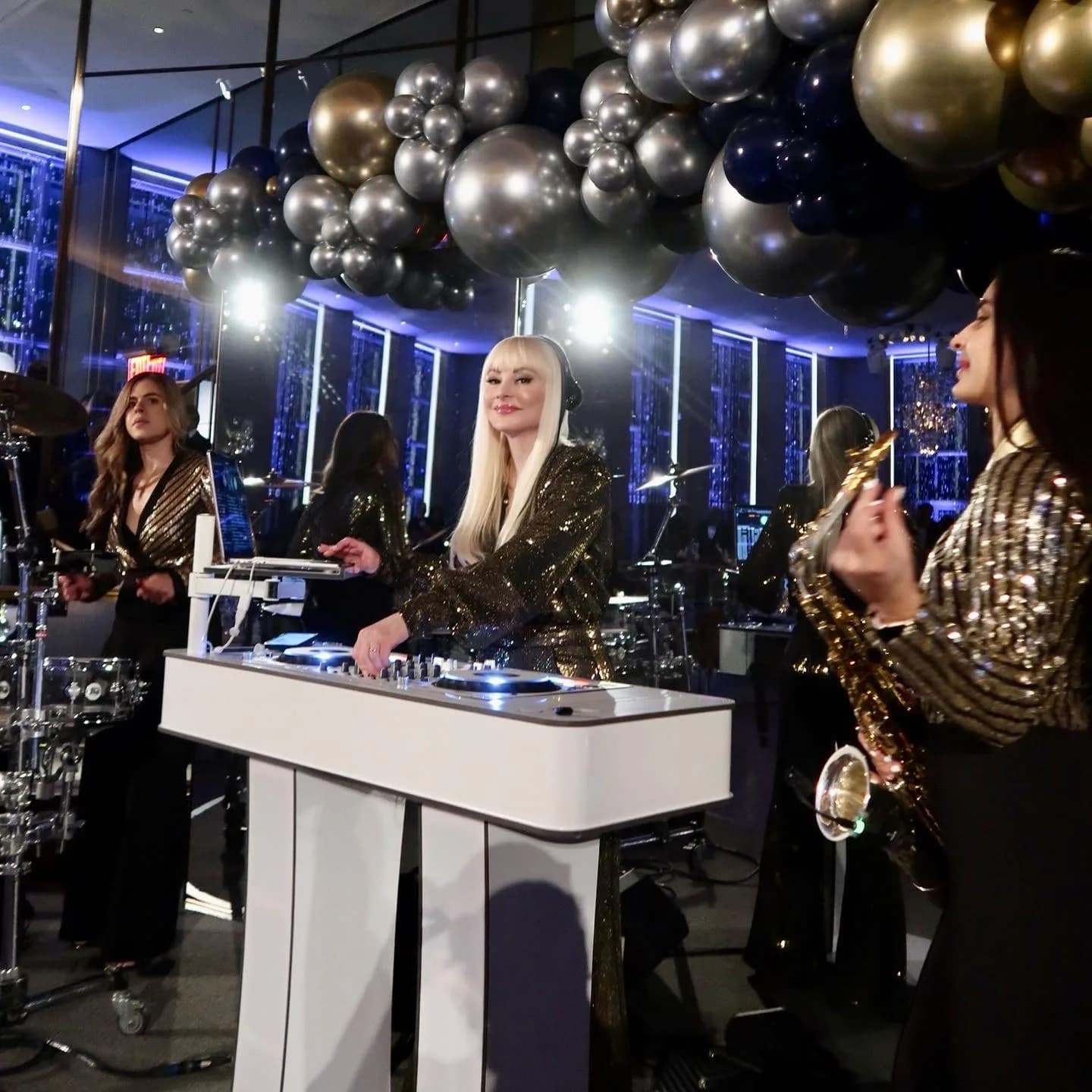 DJ Kristaval in gold sequins working the decks beneath a balloon arch at an upscale tri-state event