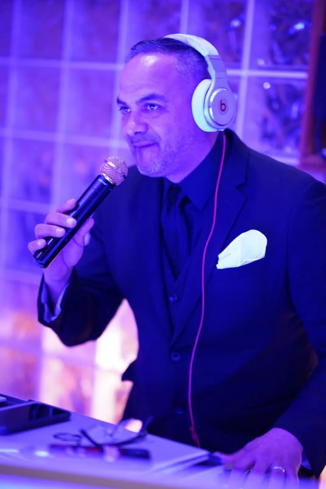 DJ and MC Omar on the microphone with headphones around his neck under purple event lighting