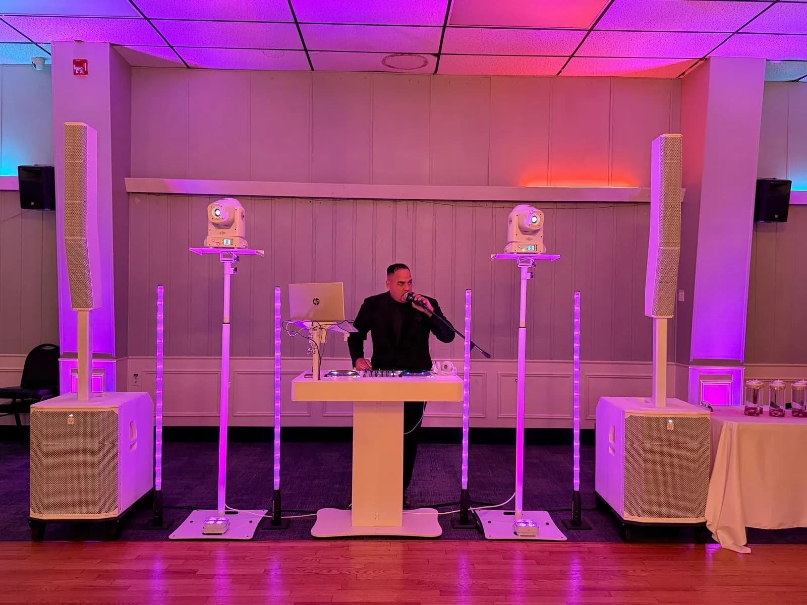 Omar's white DJ booth with LED light columns and moving head lights, shown as an atmospheric backdrop