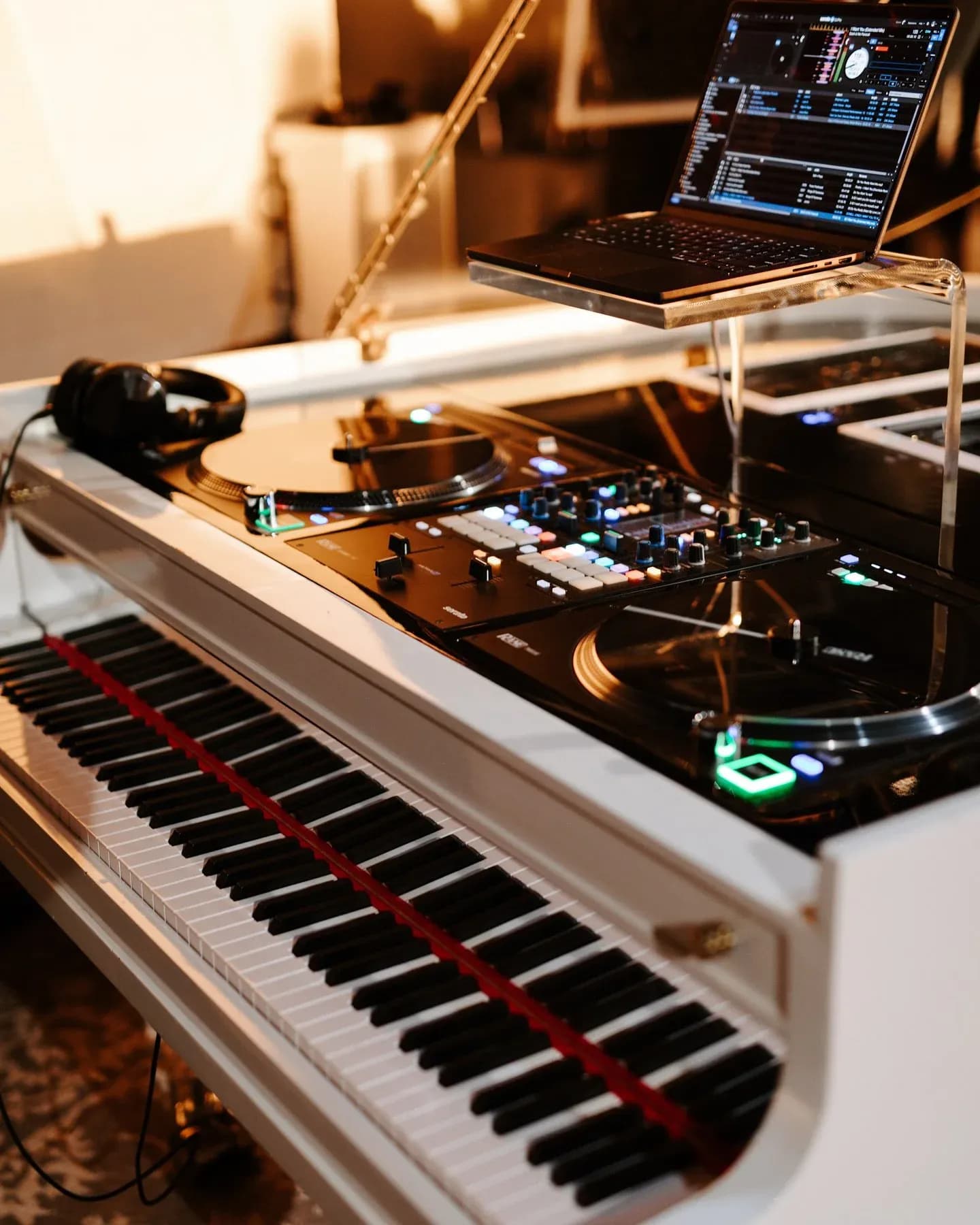Detail of the white baby grand piano DJ booth with turntables, a controller, and a laptop at an upscale event