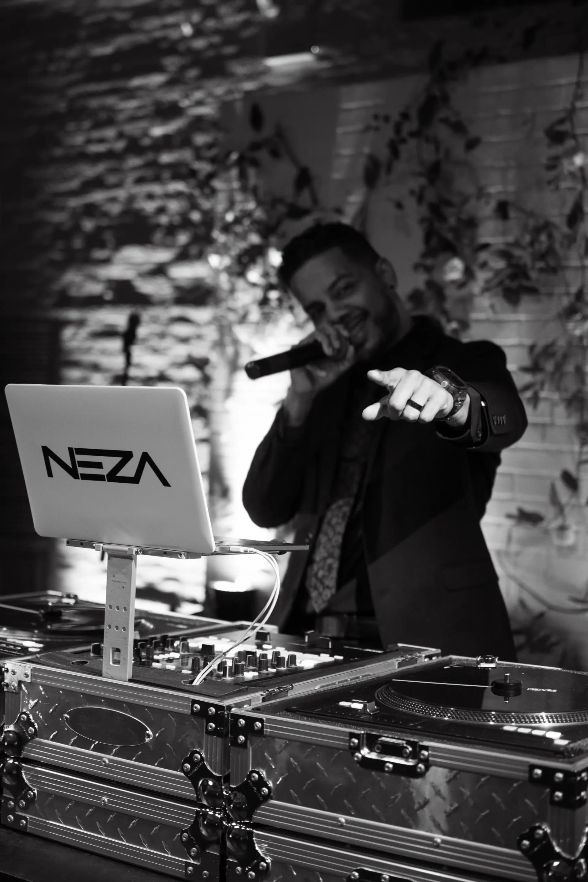 DJ Neza in black and white pointing to the crowd from behind his NEZA-branded decks
