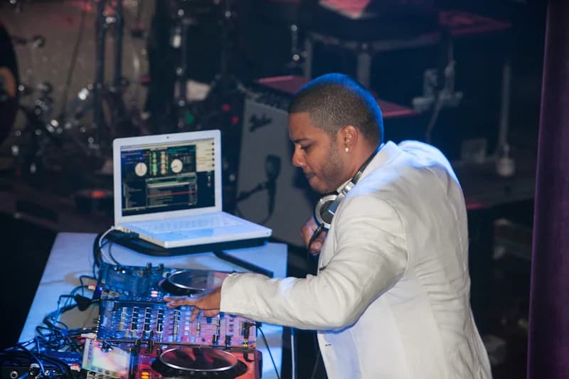DJ Neza working the decks at full focus, laptop and CDJs lit under blue venue lighting