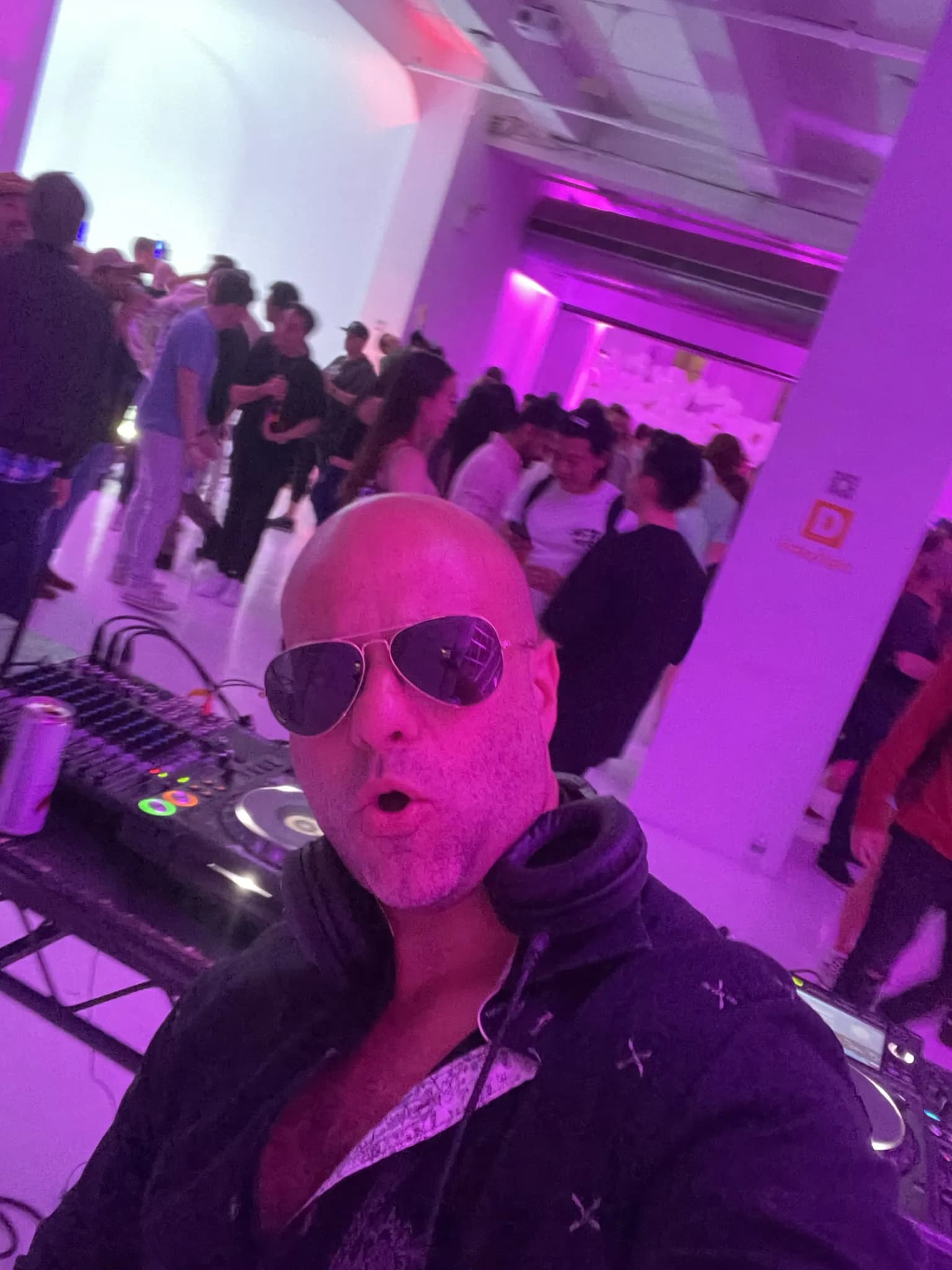 DJ Shiran Nicholson at the decks in sunglasses with a packed crowd behind him at a high-energy New York event