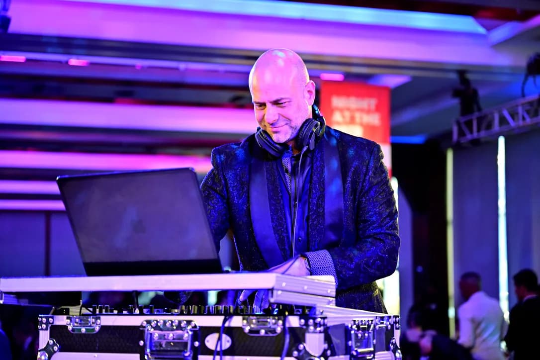 DJ Shiran Nicholson in a paisley jacket and headphones at the decks under purple light at a gala event in New York