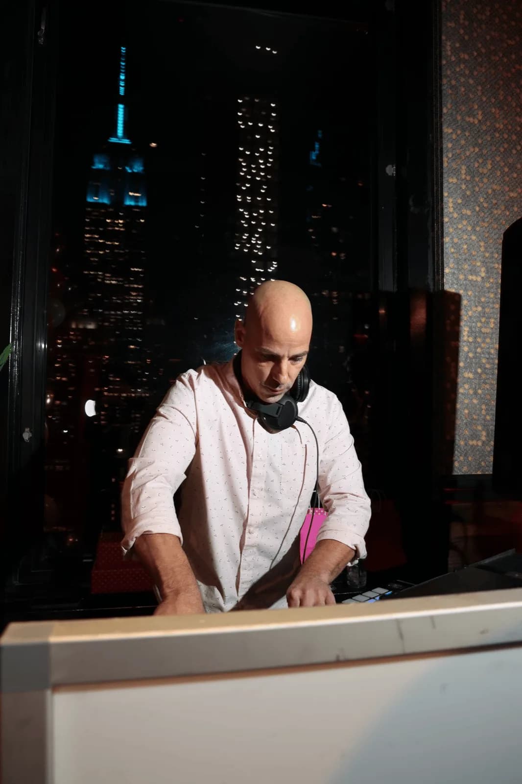 DJ Tommy at the decks against the NYC skyline at night, shown as an atmospheric backdrop