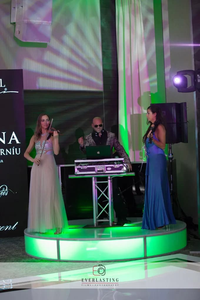 DJ Shiran on stage with two live electric violinists under green stage lighting at a Nicholson Events production