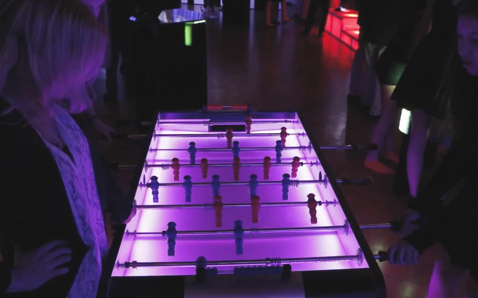 LED foosball table glowing purple at a bar mitzvah party in NYC, two players competing on the illuminated tabletop soccer surface