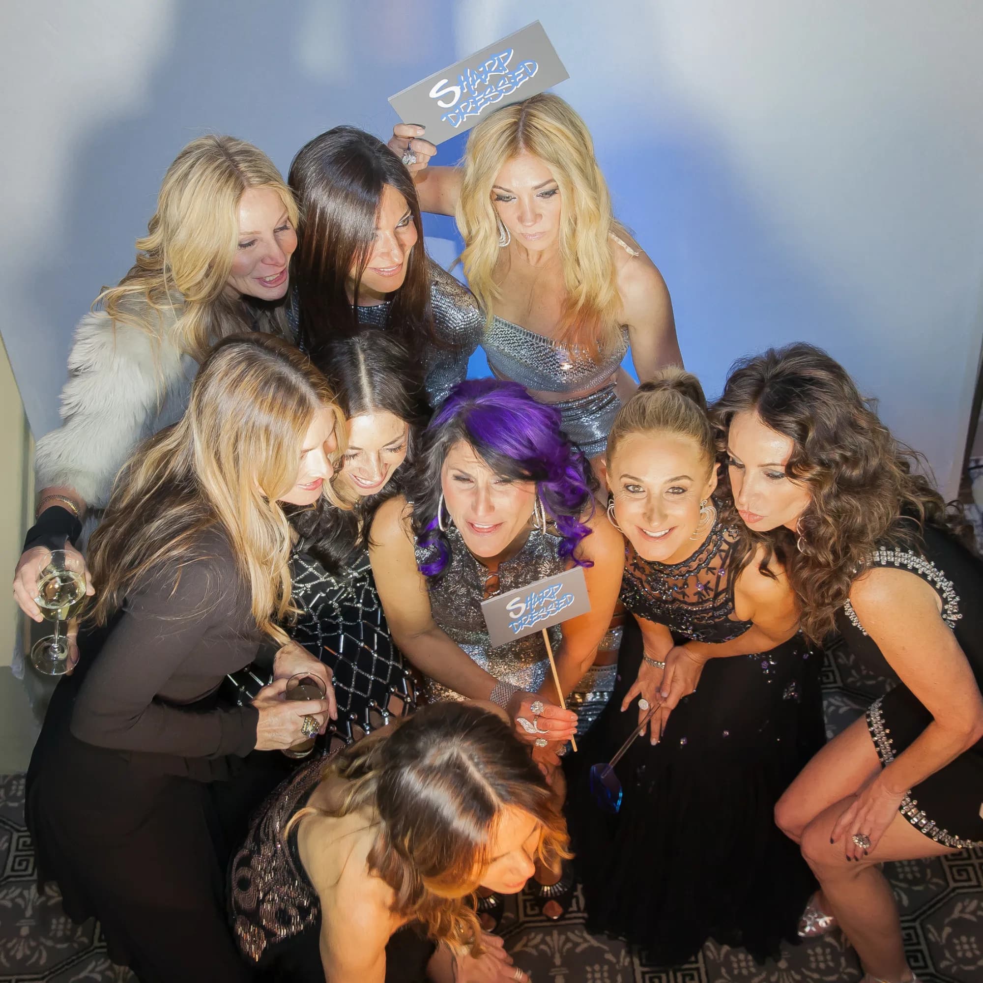 Large group of women posing together at a photo booth with custom event prop signs at a private celebration