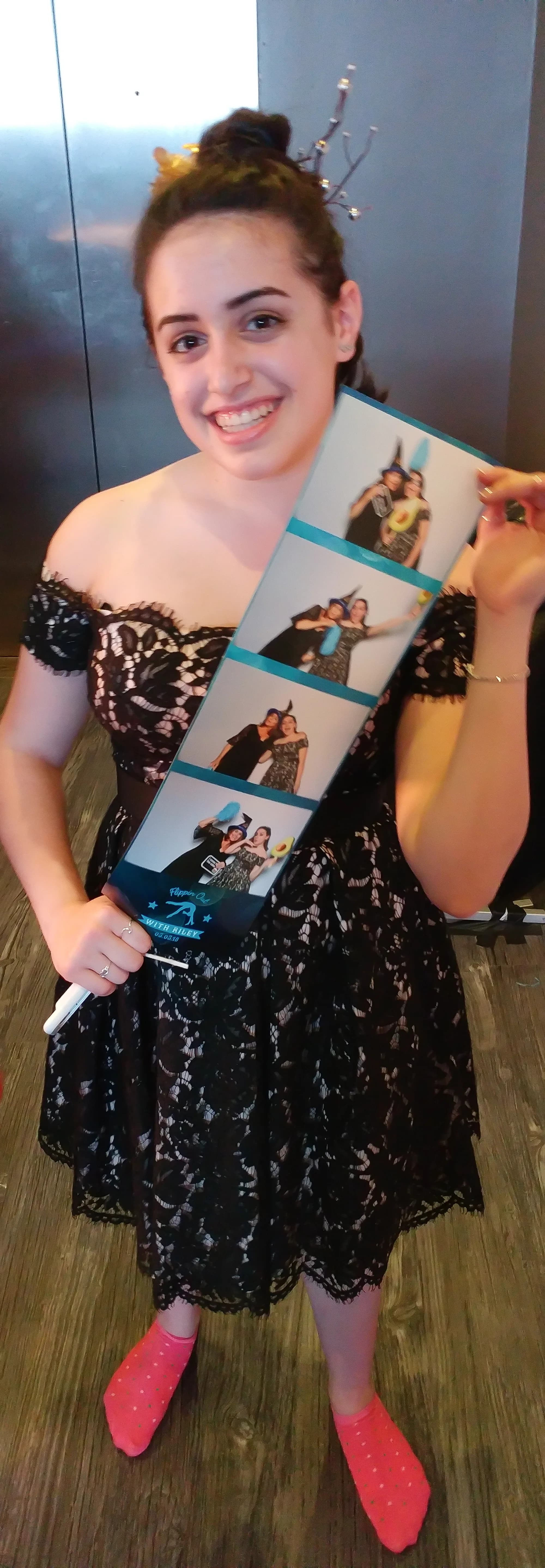 Young woman in formal attire holding an oversized photo strip print at an event, smiling proudly
