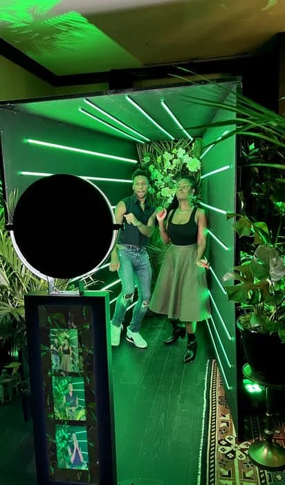 Couple posing inside a tropical neon-lit glam photo booth setup at an event venue