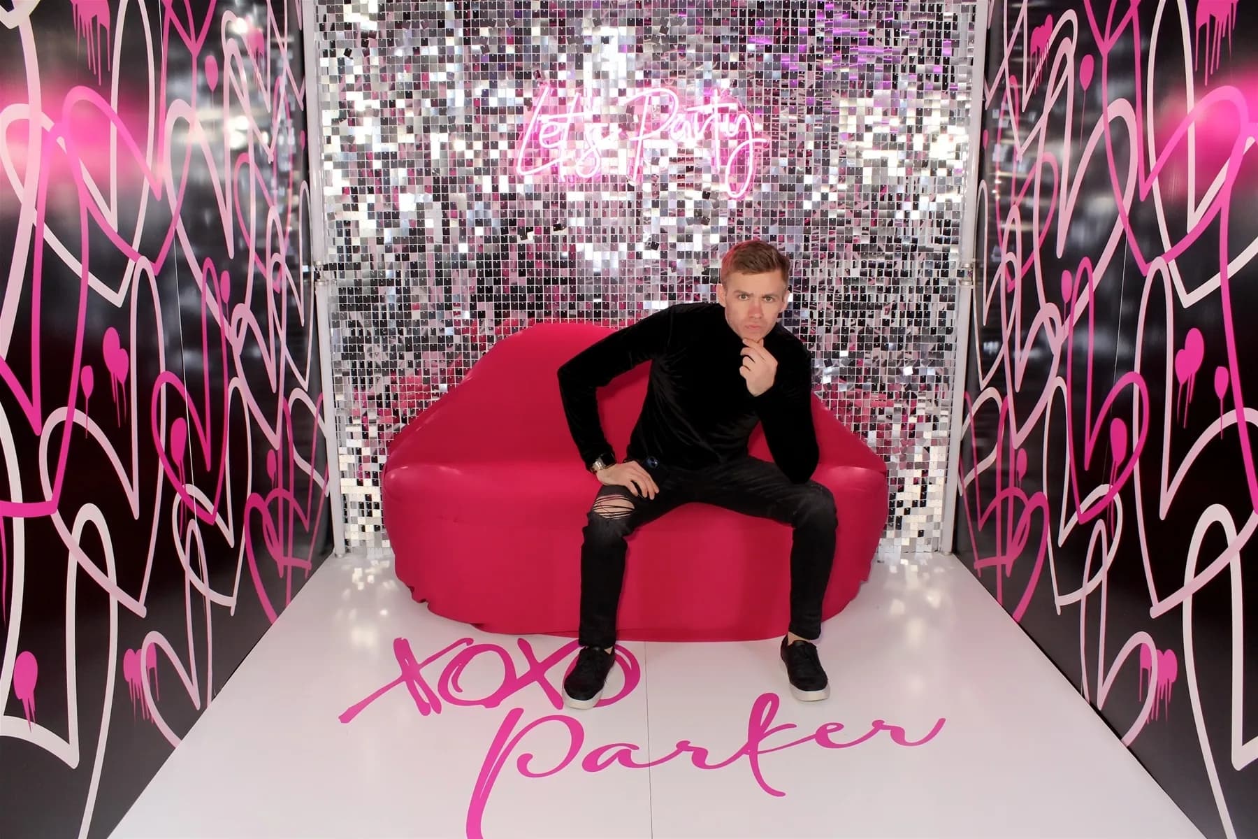 Immersive glam photo room with sequin walls, pink neon sign, and velvet couch as a styled prop for guest portraits