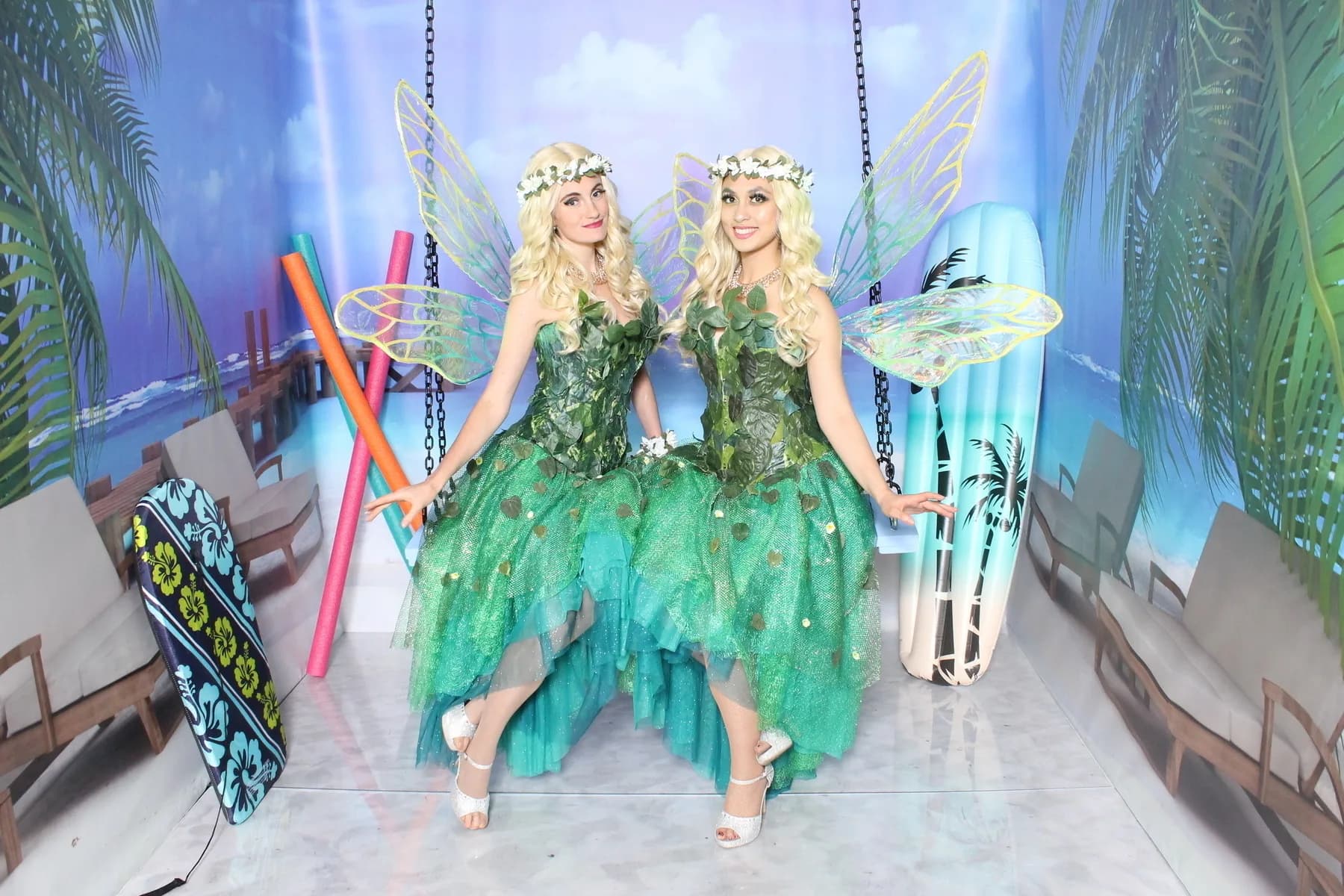 Two performers in fairy costume seated on a photo swing with a tropical backdrop inside an immersive themed room