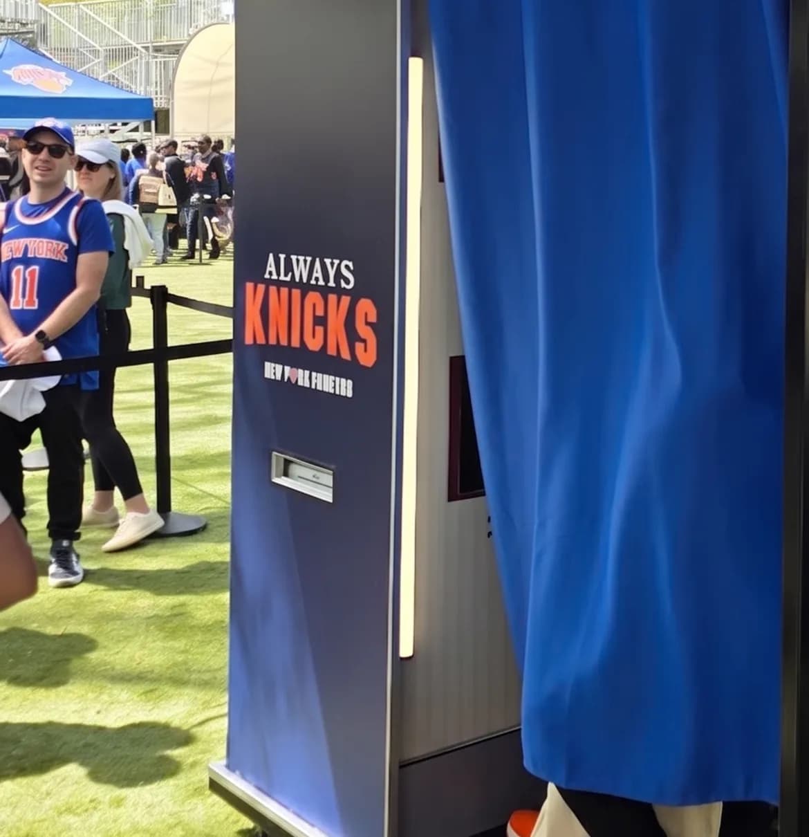 Guests in team jerseys waiting in line beside the blue curtain entrance of a vintage sports photo booth