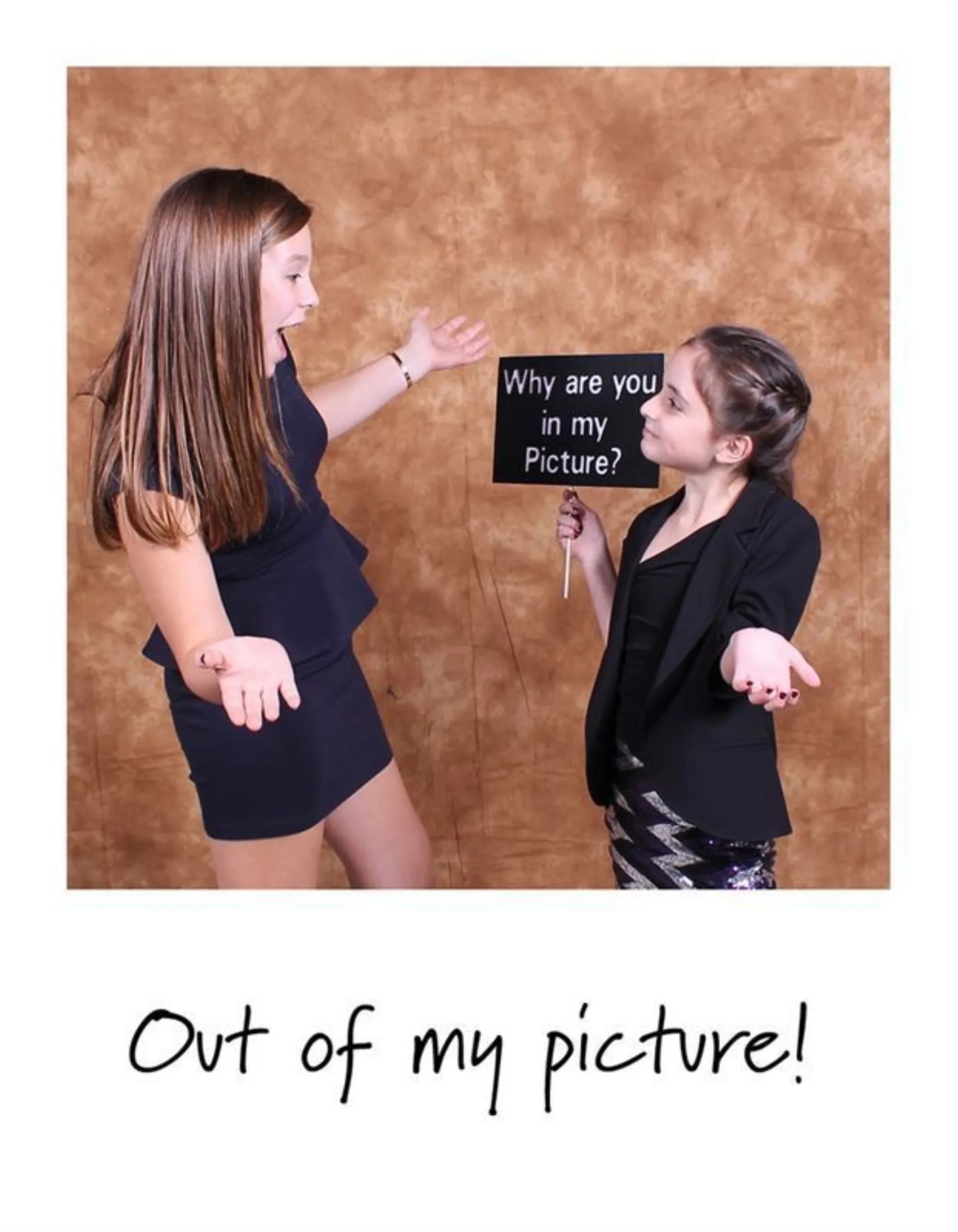 Two guests posing playfully with a Polaroid-format print and a fun photo prop sign at an event