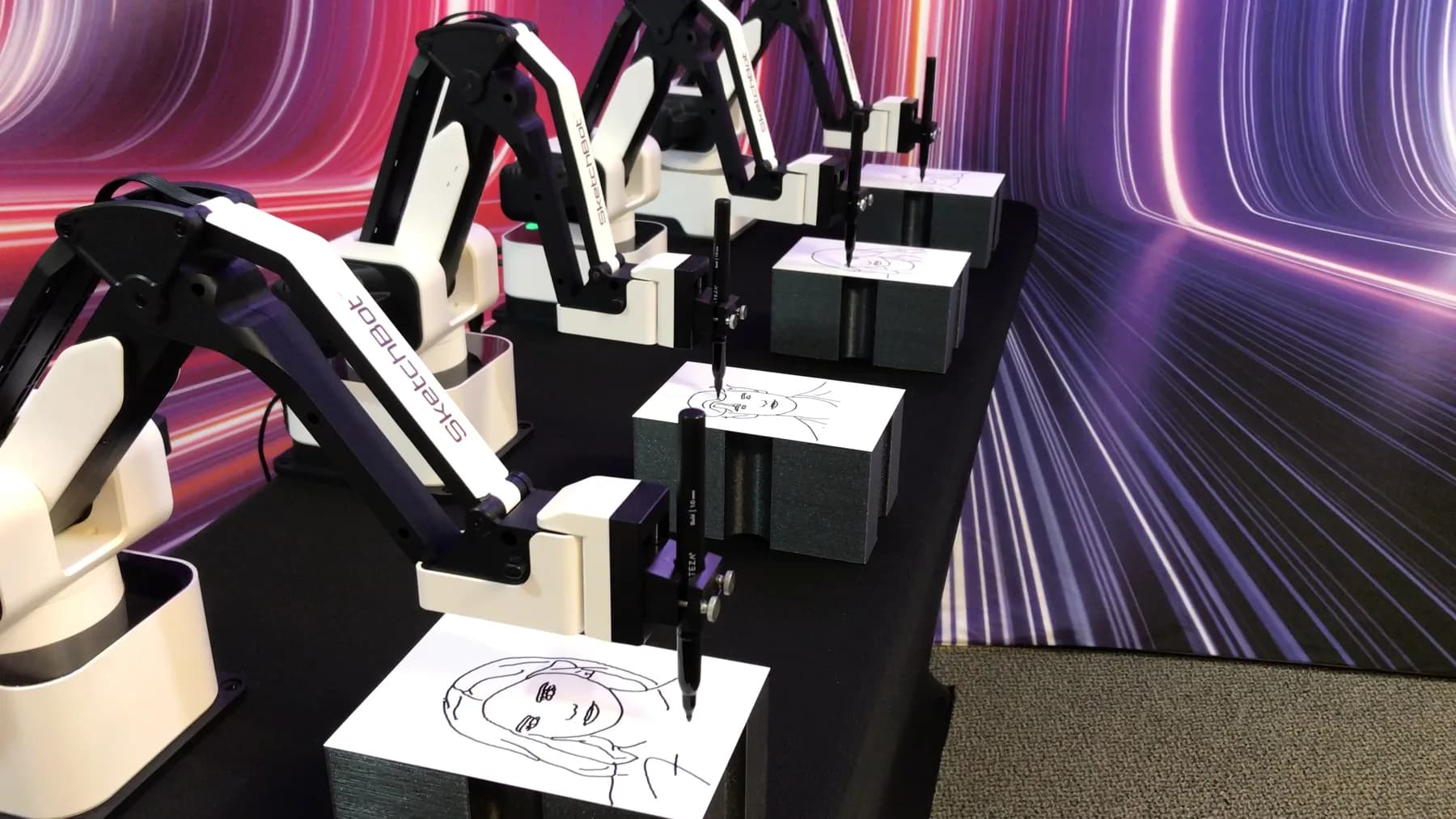 Multiple SketchBot robot arms drawing simultaneously against a vivid purple and pink light backdrop