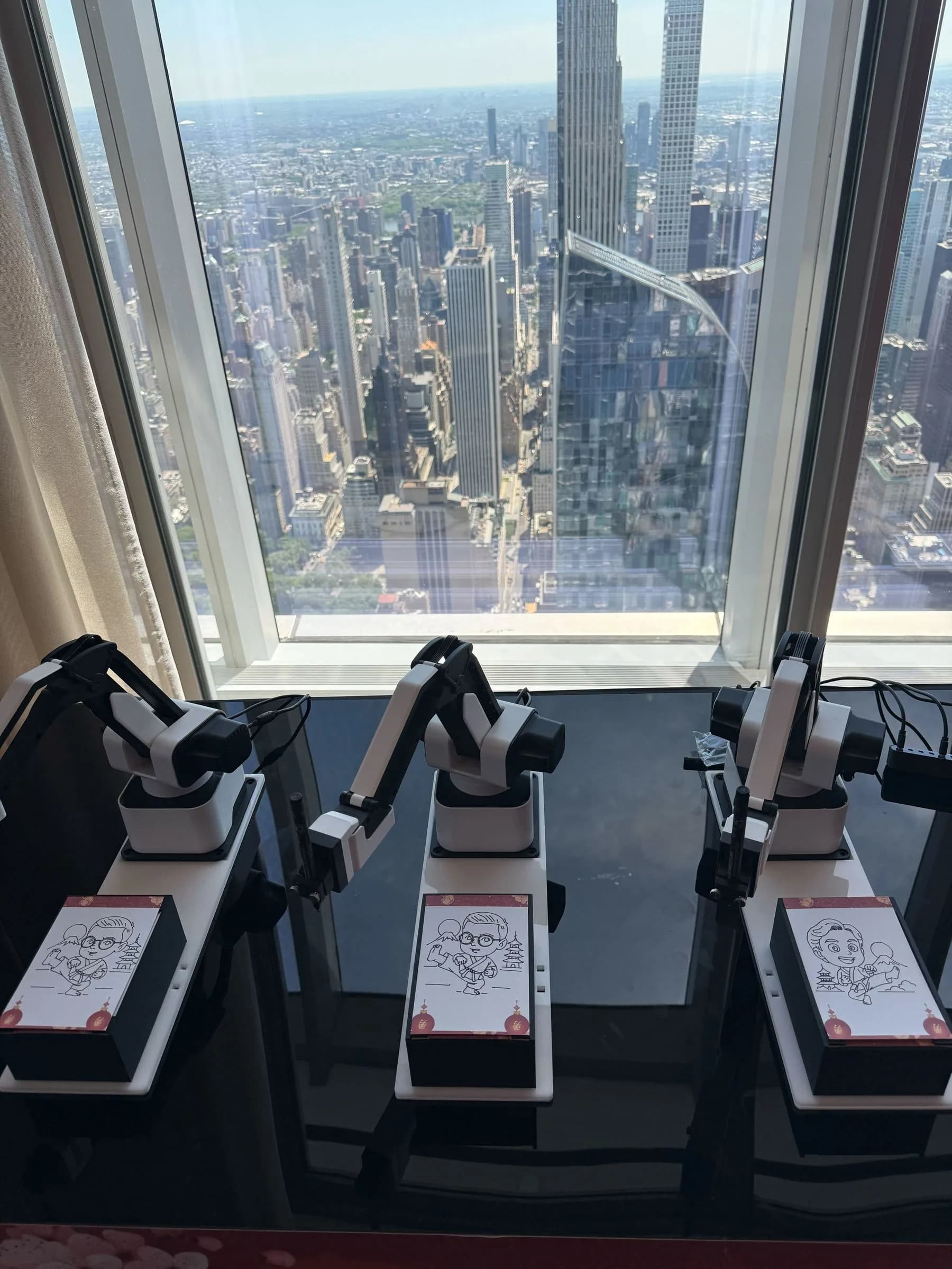 SketchBot robotic arms drawing AI portraits mid-session with NYC cityscape through the window