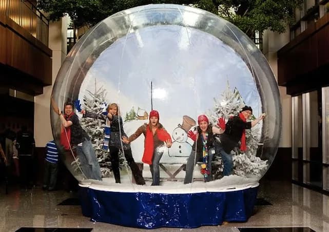 Guests gathered inside a giant walk-in snow globe with artificial snow swirling around them