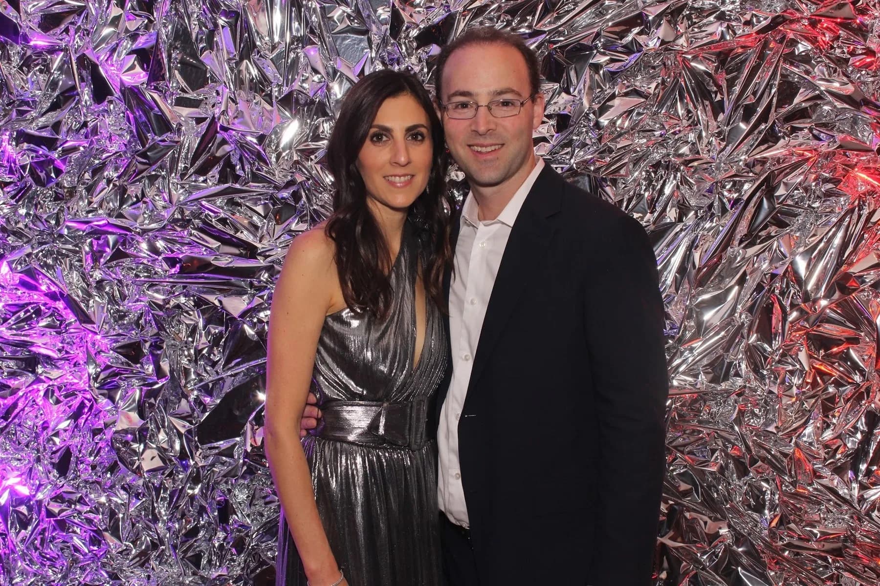Couple posing against a silver crinkle foil wall with colored ambient lighting at a formal event
