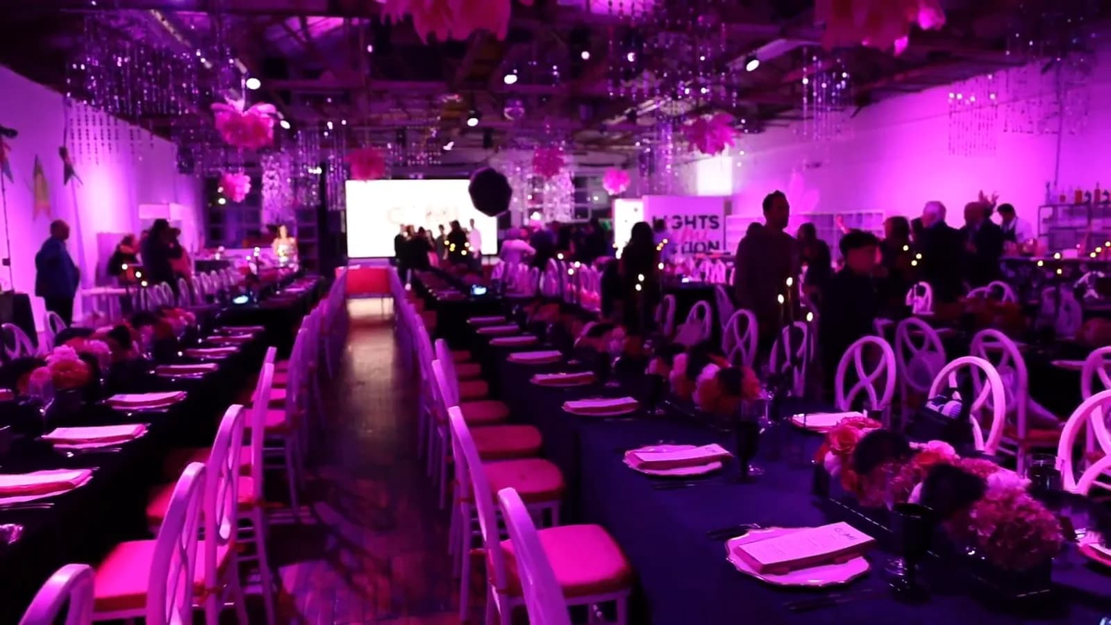 Long banquet tables dressed for a festive seated dinner with vivid uplighting in the Boathouse at The Knowlton in Bridgeport, CT