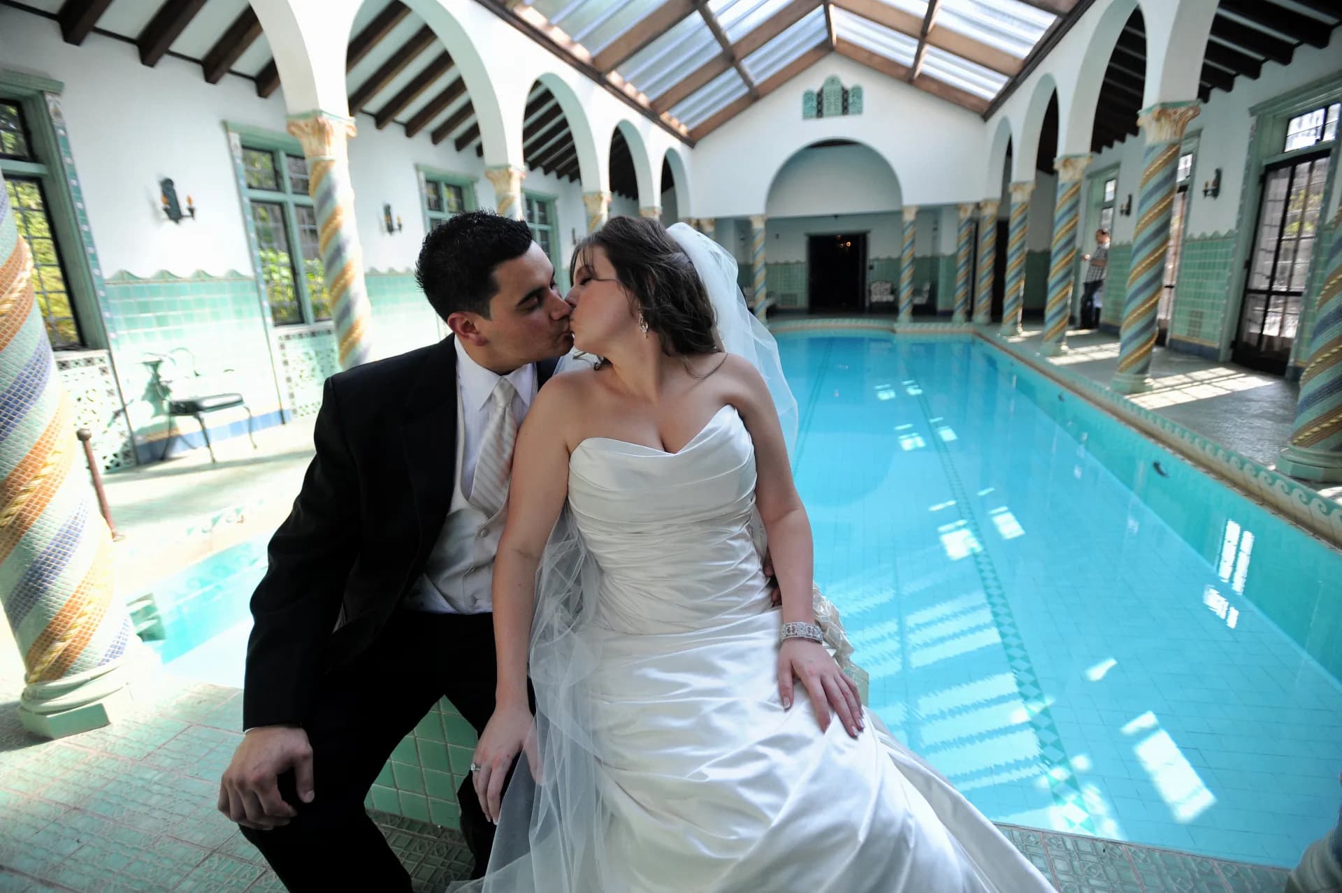 Bride and groom kissing beside the pool in an ornate indoor pool pavilion