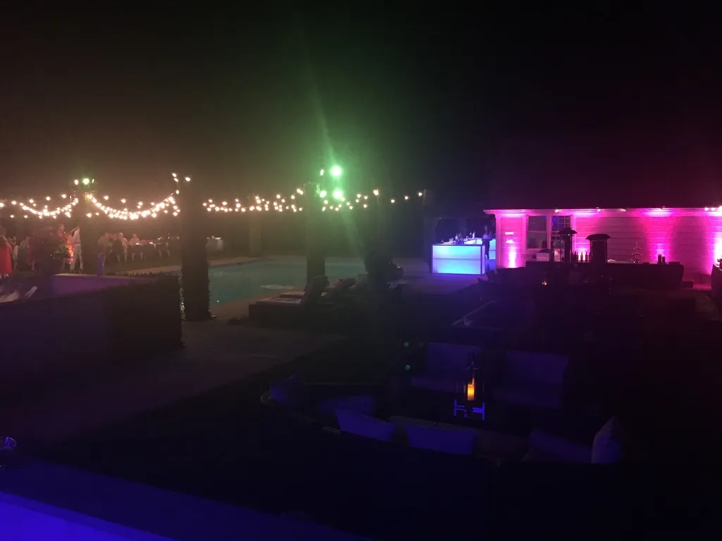Hamptons estate pool party at night with colored uplighting and a lit bar by Nicholson Events