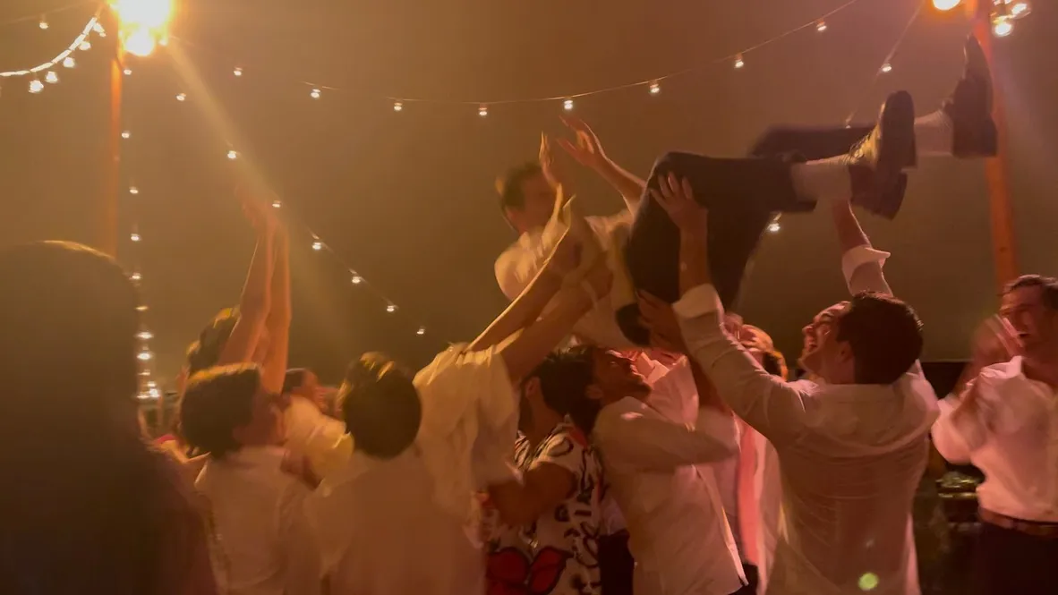 Guests lifting the guest of honor in a hora under tented string lights at a Hamptons summer party