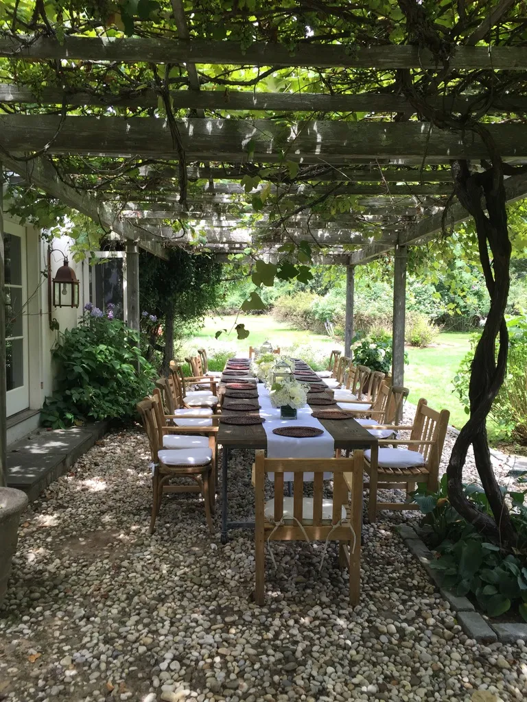 Al fresco dining table set under a vine covered pergola at a Hamptons summer party by Nicholson Events